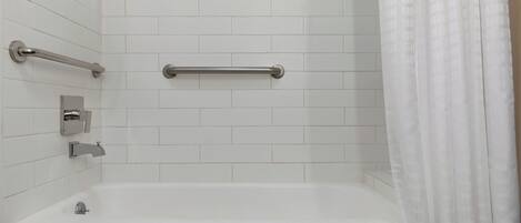 A bathroom with white tiles, a bathtub, a handrail, and a shower curtain.