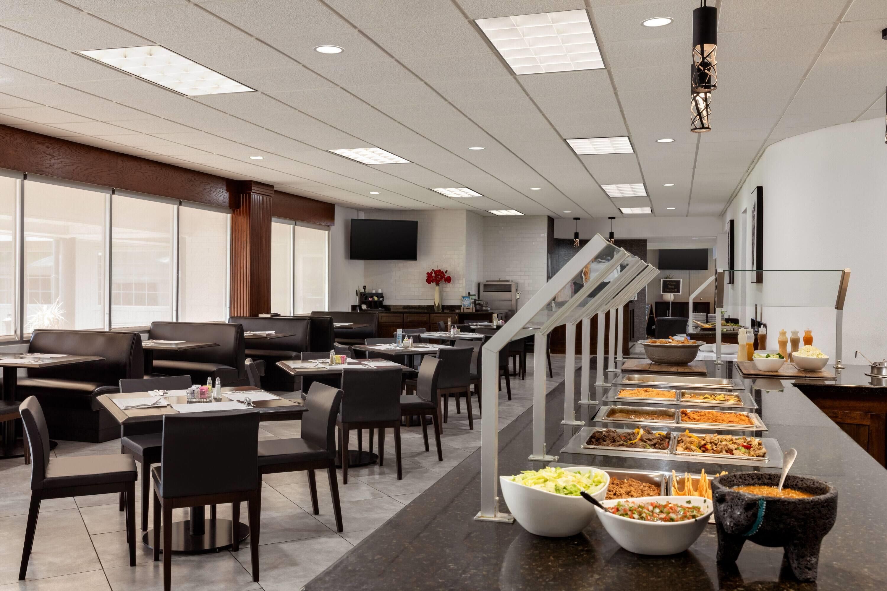 Un comedor moderno con cabinas y mesas, un bufé con diversas opciones de comida, y una escalera que conduce a otro nivel.