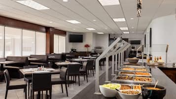 Un comedor moderno con cabinas y mesas, un bufé con diversas opciones de comida, y una escalera que conduce a otro nivel.