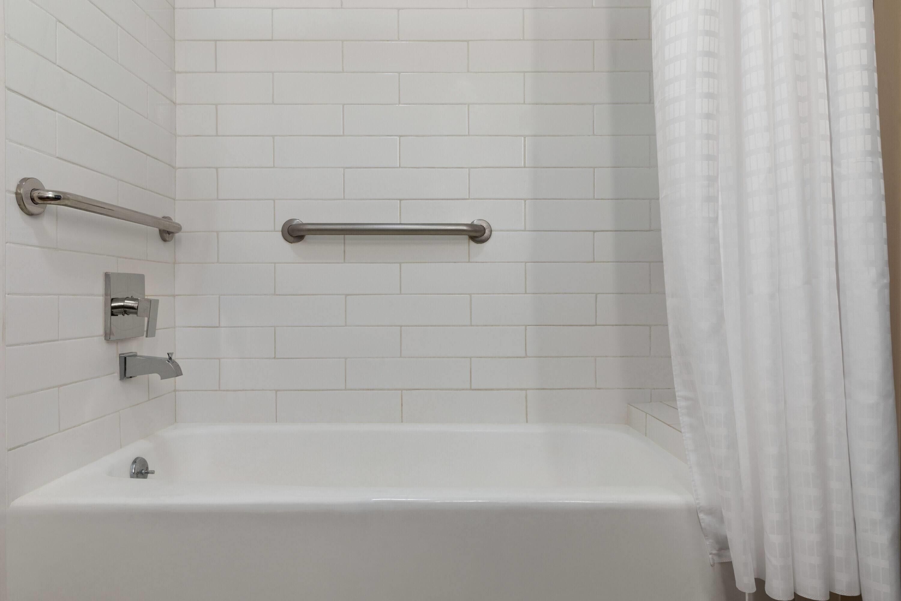 A modern bathroom with white tiles, a bathtub, a shower curtain, and a grab bar.