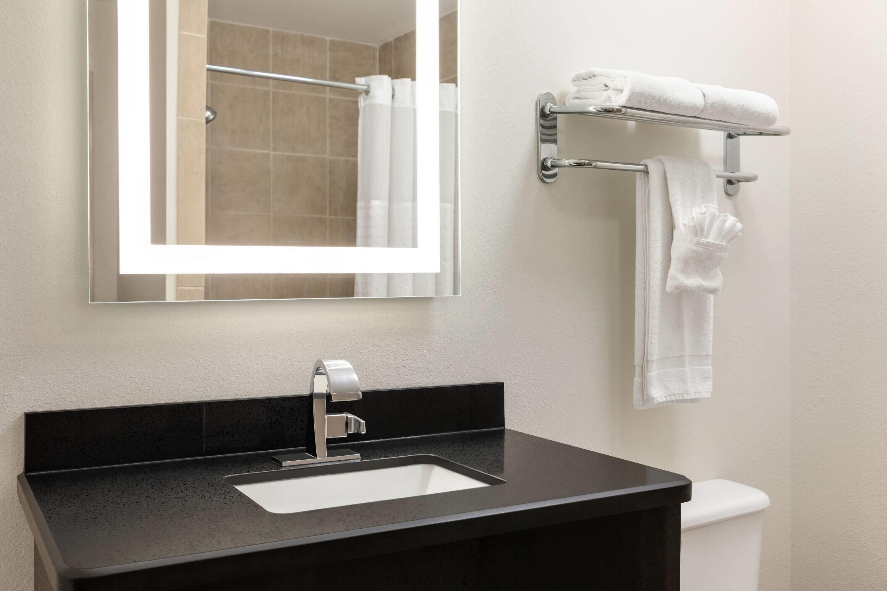A modern bathroom with a black sink, a mirror, and a towel rack with towels.