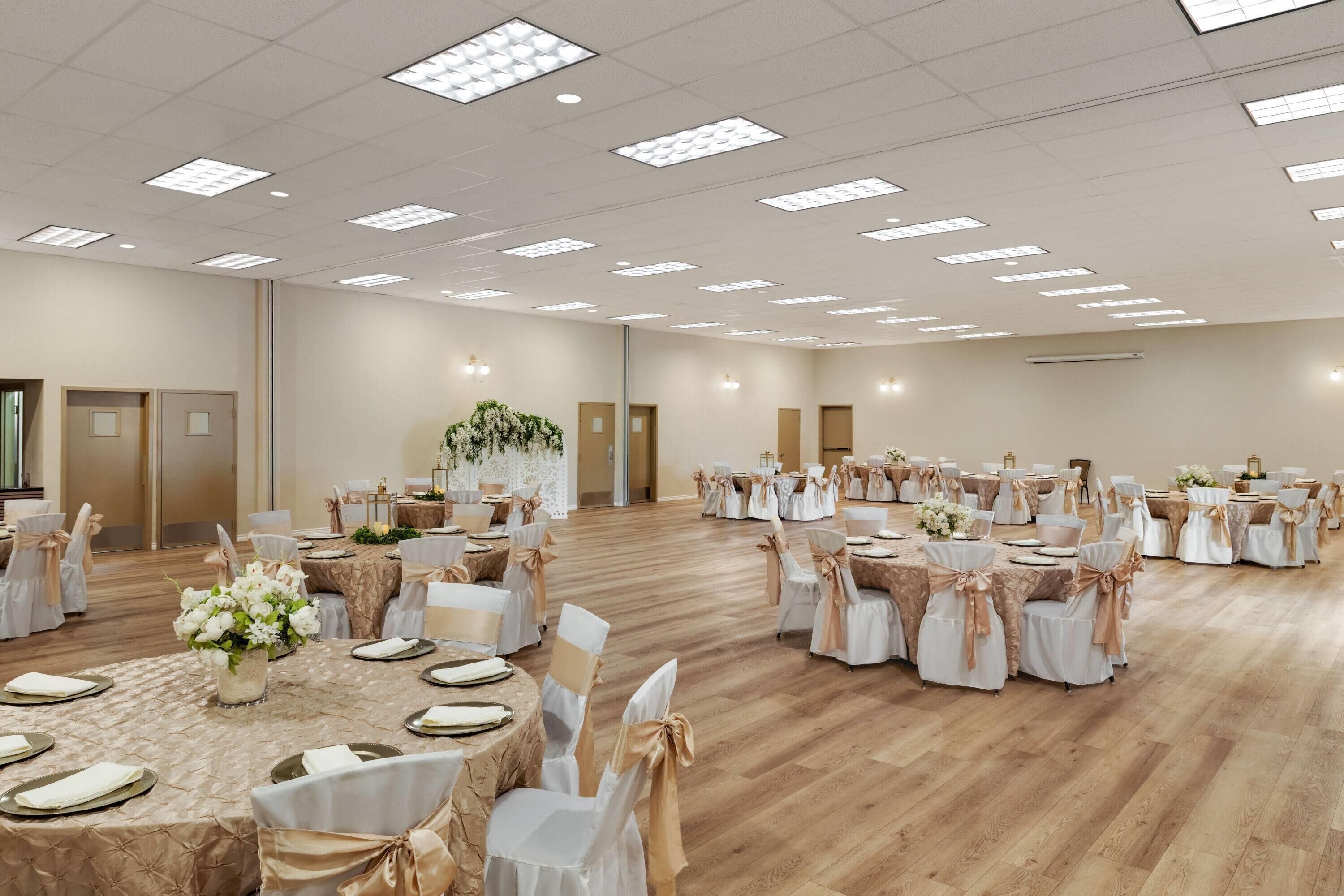 A large banquet hall with round tables, white chairs, and floral centerpieces.