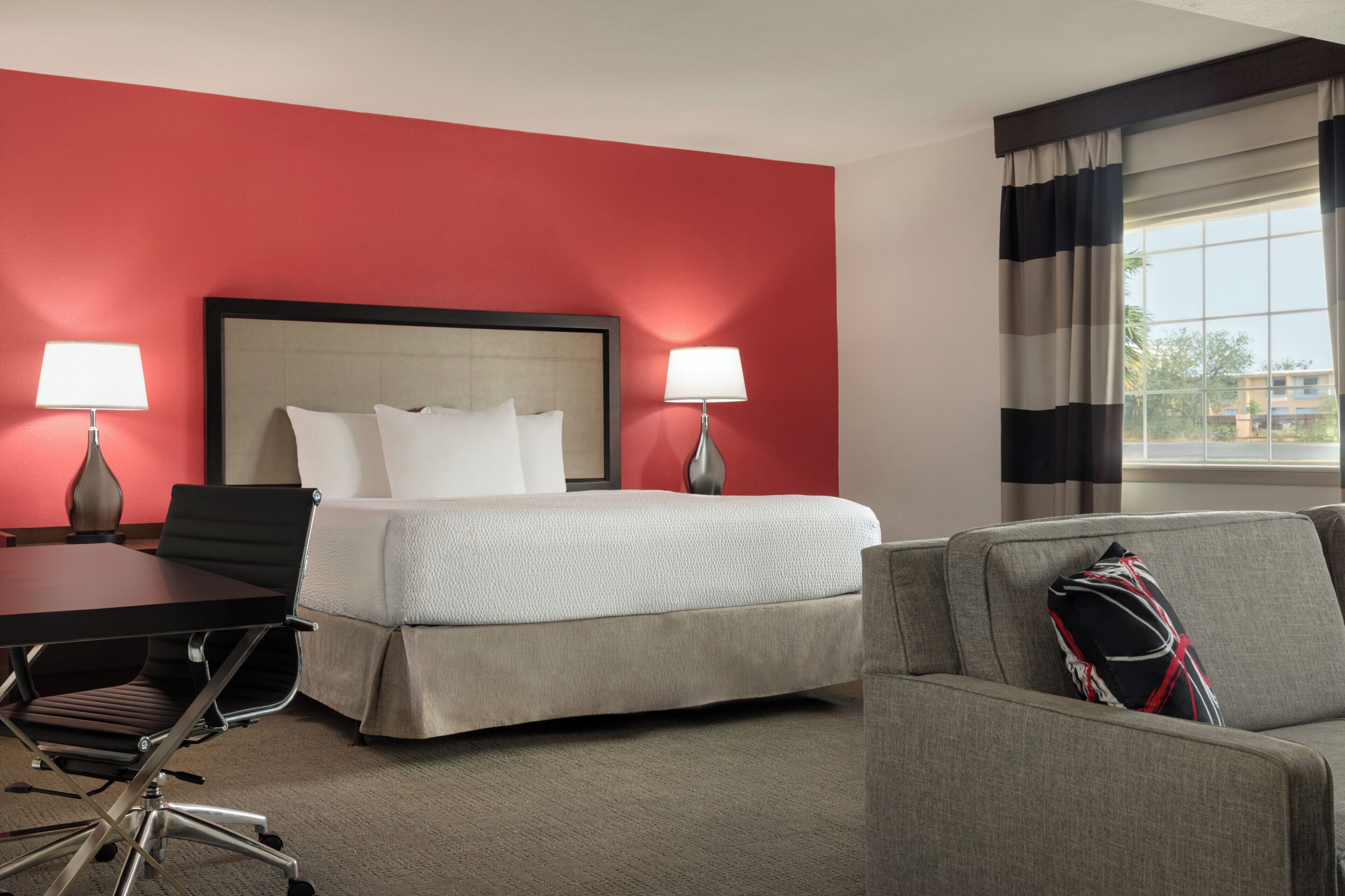 A hotel room with a bed, two bedside lamps, a desk with a chair, and a sofa.