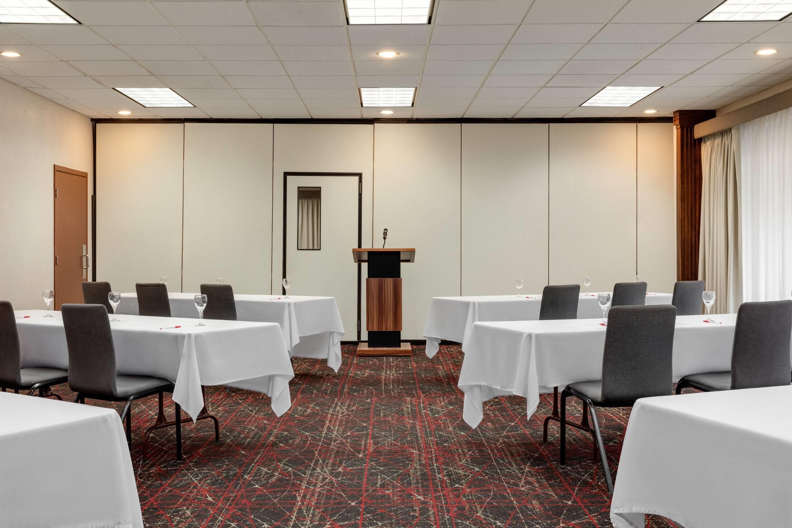 Une salle de conférence équipée de tables et de chaises, d’un pupitre et d’un sol recouvert de moquette.