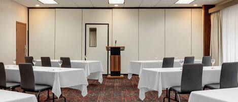 Une salle de conférence équipée de tables et de chaises, d’un pupitre et d’un sol recouvert de moquette.