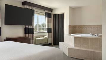 Une chambre d’hôtel avec un grand lit, un téléviseur à écran plat, une baignoire et une fenêtre avec des rideaux.