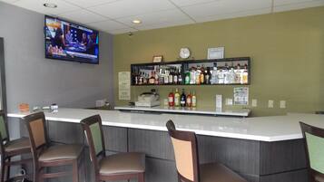A bar area with a counter, stools, a television screen, and a shelf with bottles.