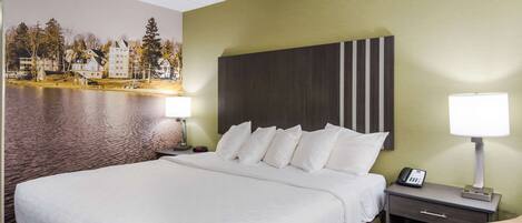 Una habitación de hotel con una cama grande, una mesita de noche con lámpara, un teléfono y un televisor montado en la pared.