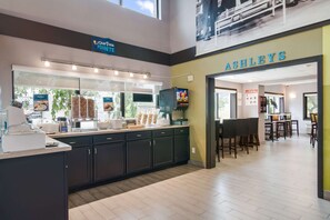 A modern cafe with a counter displaying food items, a dining area with tables and chairs, and a sign for 'Ashley’s' on the wall. - Clarion Pointe Jamestown - Falconer (Jamestown)