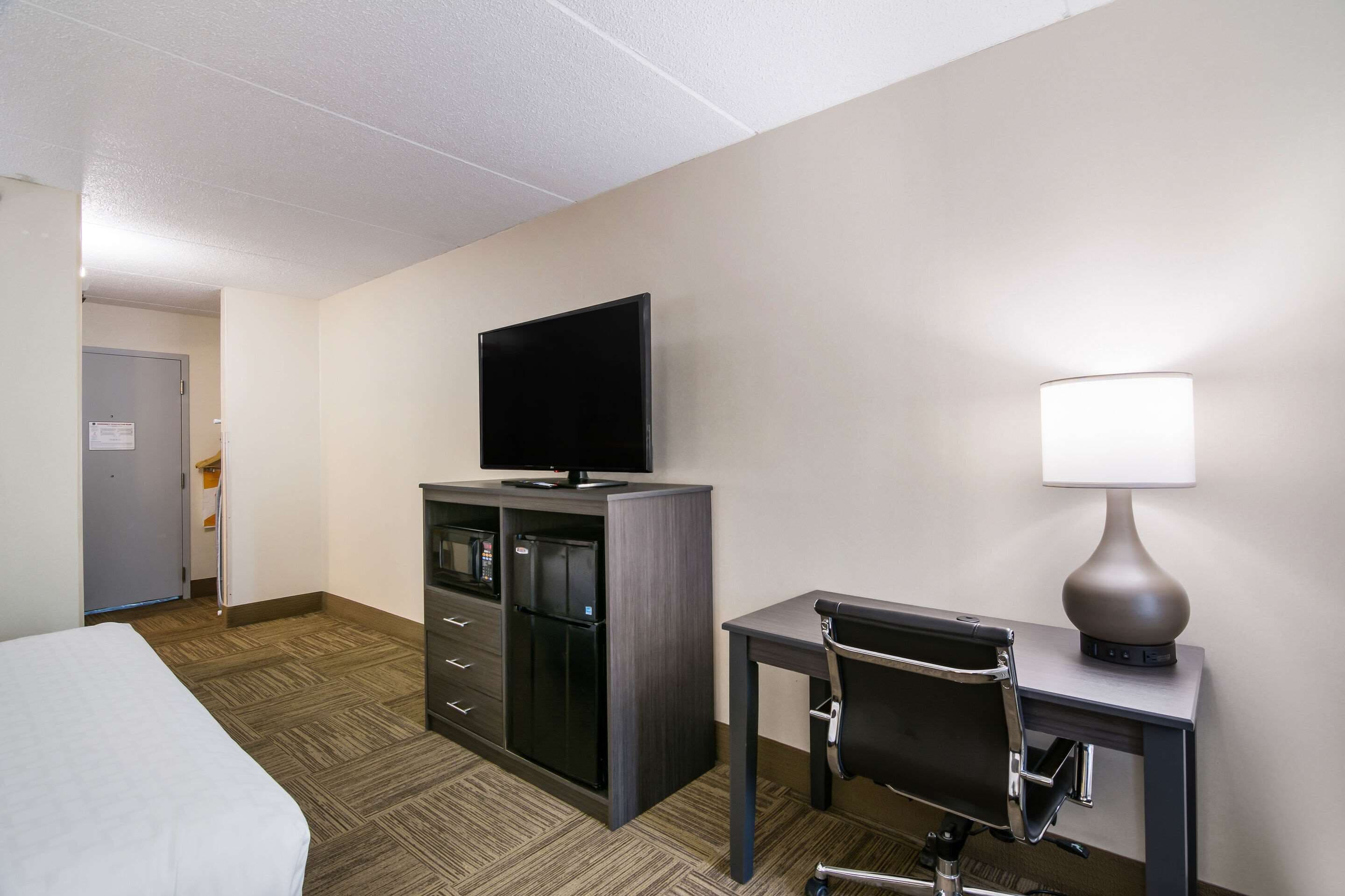 Habitación de hotel con cama, escritorio con silla, televisión, minibar y lámpara.