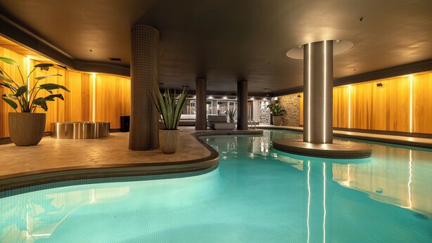 A swimming pool with a tiled floor, surrounded by wooden walls and columns, and potted plants.