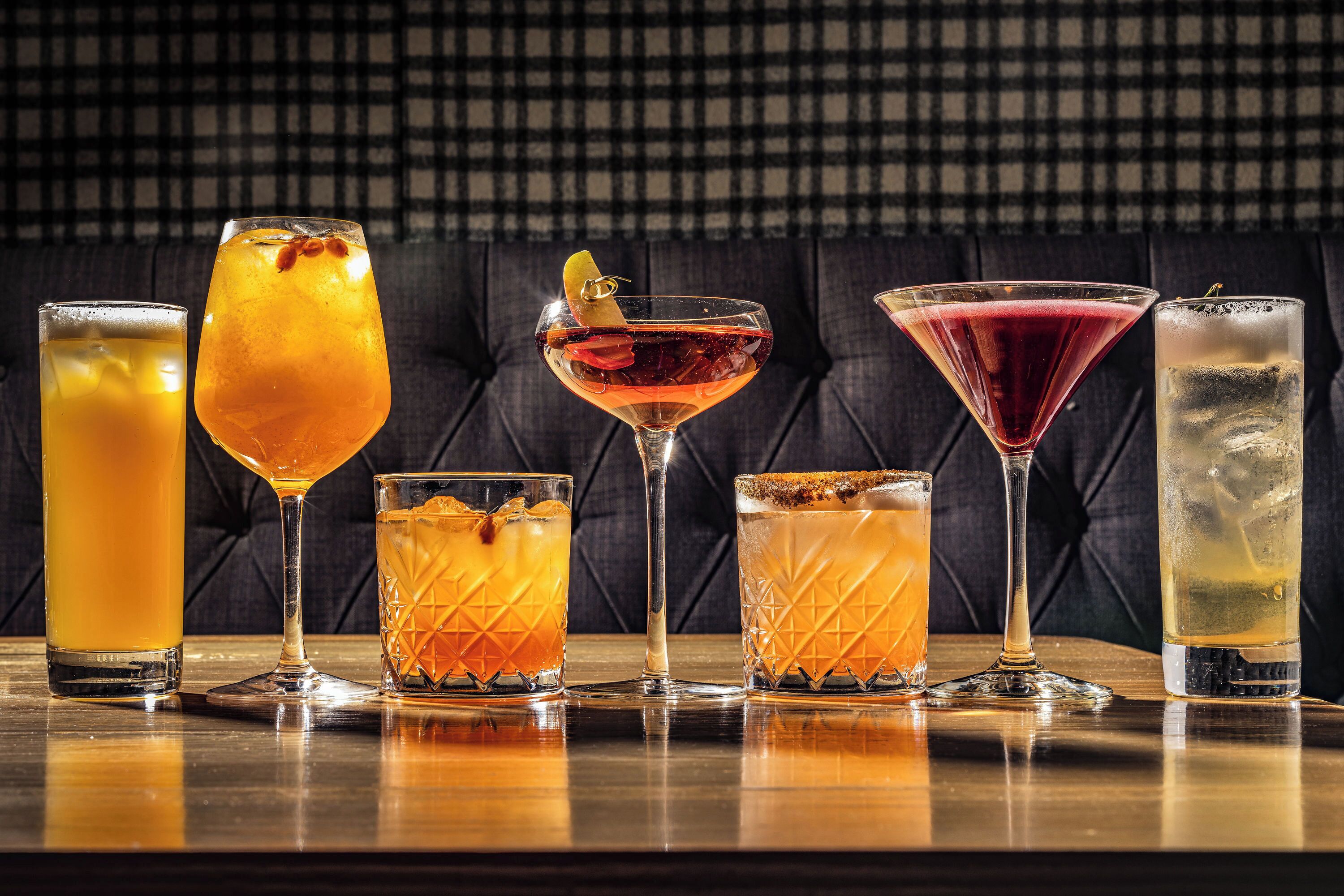 A variety of drinks in different glassware on a wooden table against a checkered background.