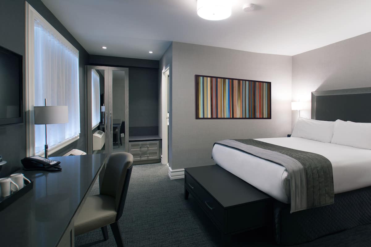 Une chambre d’hôtel avec un grand lit, un bureau avec un téléphone, une chaise et une table de chevet avec une lampe.