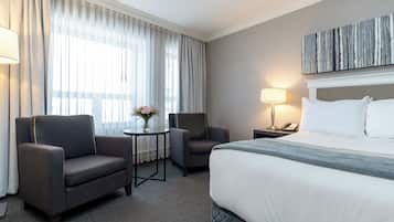 Habitación de hotel con una cama grande, dos sillones, una mesita con un jarrón, una lámpara y un cuadro en la pared.
