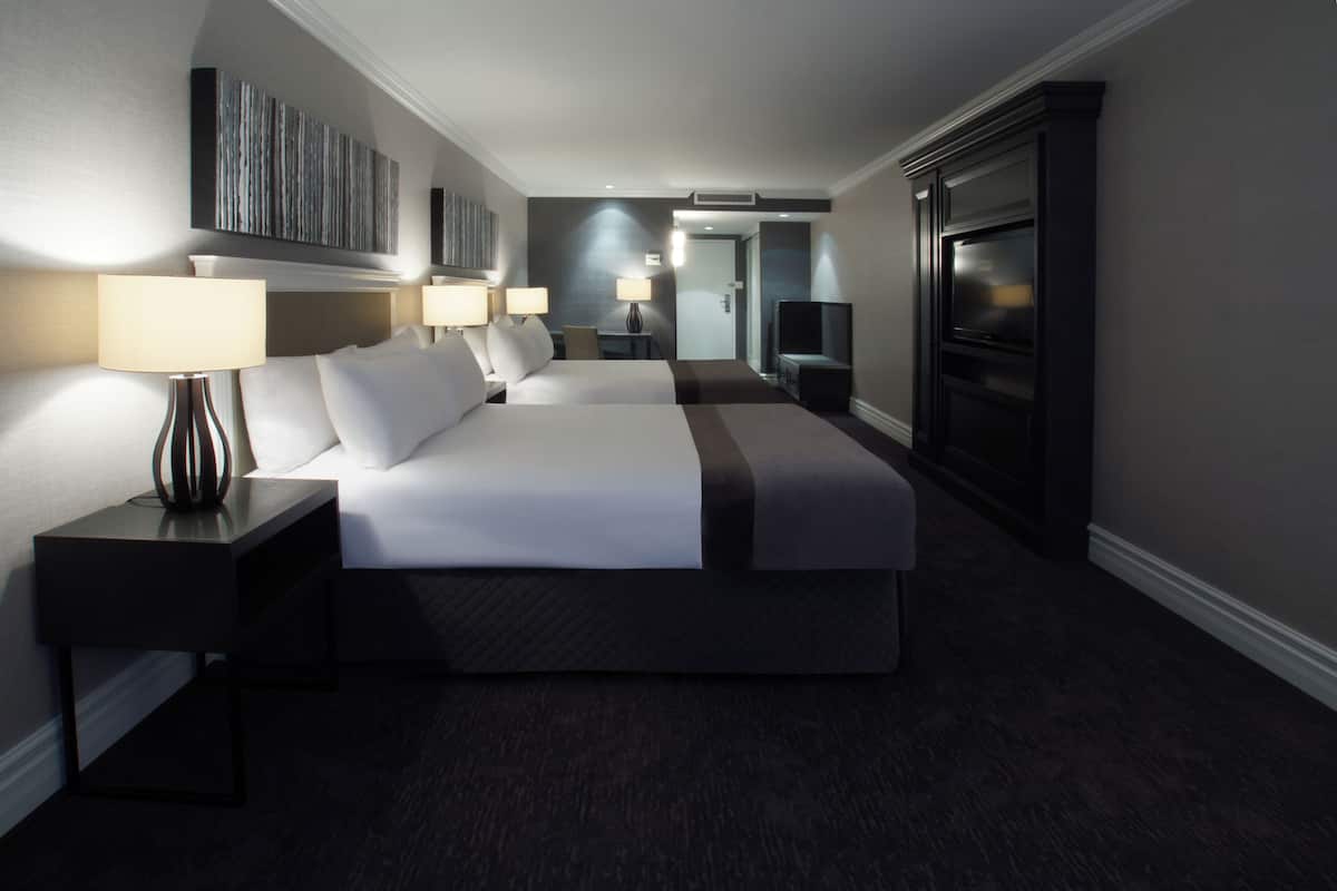 Une chambre d’hôtel moderne dotée d’un grand lit, de deux tables de chevet avec des lampes, d’un téléviseur à écran plat et d’un grand miroir.