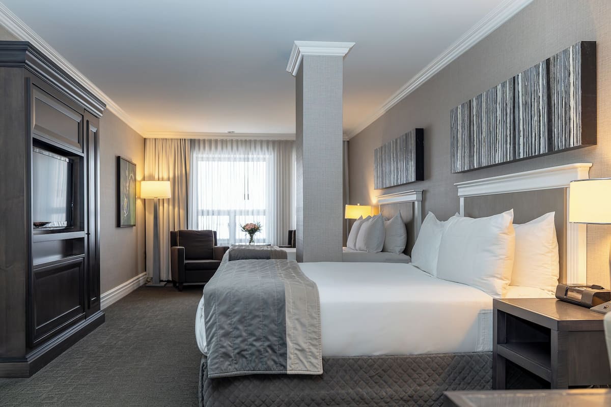 Une chambre d’hôtel avec un grand lit, un bureau, une chaise, une télévision et une fenêtre avec des rideaux.