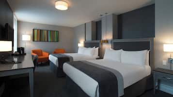 A hotel room with two beds, a desk with a telephone, two chairs, a coffee machine, and a colorful abstract painting on the wall.
