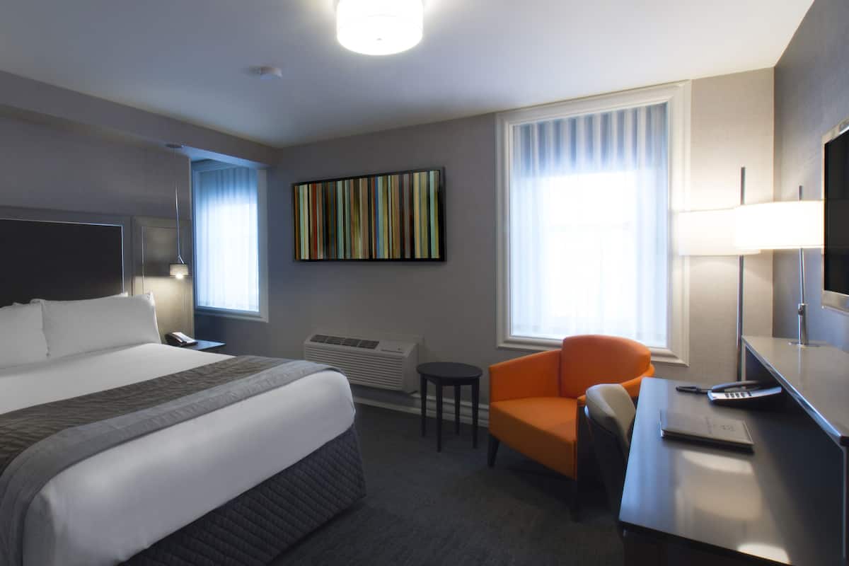 Une chambre d’hôtel avec un grand lit, un bureau avec une chaise, une télévision et une fenêtre avec des rideaux.