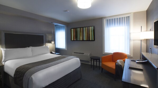 A hotel room with a large bed, a desk with a chair, a TV, and a window with curtains.