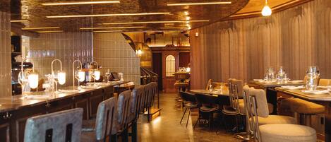 Un interior de restaurante con una barra larga, varias mesas y sillas.