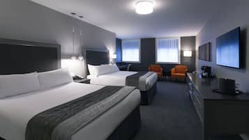 A hotel room with two beds, a desk, a chair, and a TV.