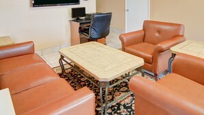 A room with a flat-screen TV, a desk, a computer, a chair, and a sofa. - Super 8 by Wyndham Decatur Texas (Decatur)