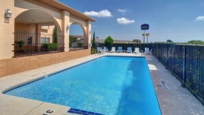 A rectangular swimming pool with a tiled edge, a brick building with a covered patio area, and a fenced poolside with lounge chairs. - Super 8 by Wyndham Decatur Texas (Decatur)