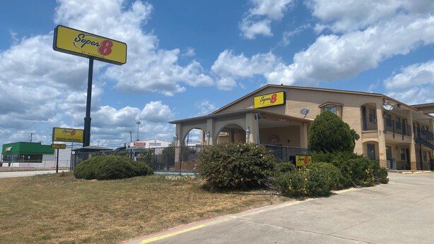 A Super 8 motel with a parking lot, a green building in the background, and a clear sky.