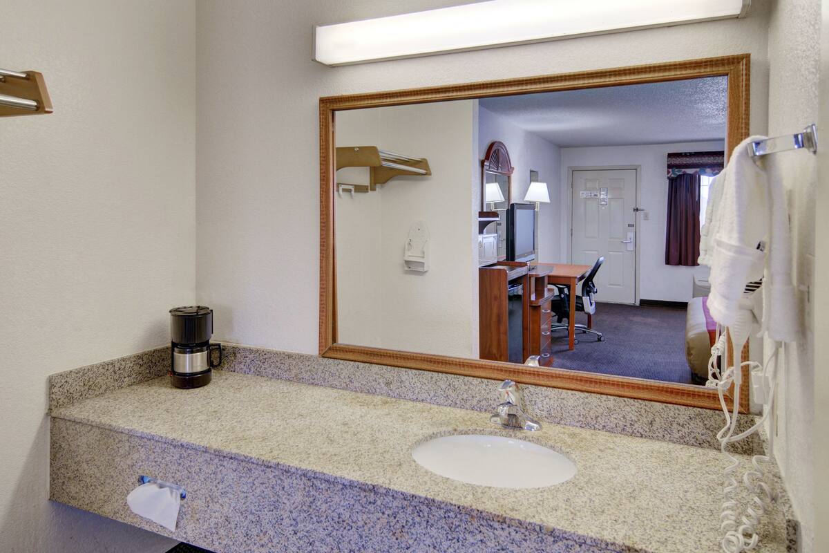 A hotel bathroom with a granite countertop, a sink, a mirror, a hairdryer, and a coffee maker.