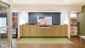 Ein Hotelrezeptionstresen mit Holzausstattung, ein großes abstraktes Gemälde darüber, eine Minibar und ein Snackbar zur Rechten.