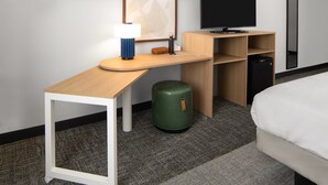 Ein Hotelzimmer mit Schreibtisch, Flachbildfernseher, Bett und einem grünen Mülleimer.