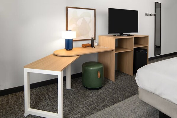Habitación de hotel con escritorio, televisor de pantalla plana, cama y un bote de basura verde.