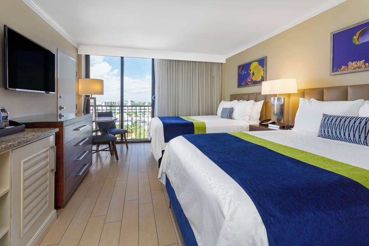Habitación de hotel con dos camas, un escritorio, un televisor y un balcón con vistas.