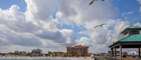A coastal hotel with a beach view, a pier, and a large building with a red roof.