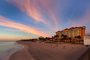 Un hotel frente a la playa con un edificio grande, palmeras y una playa de arena.