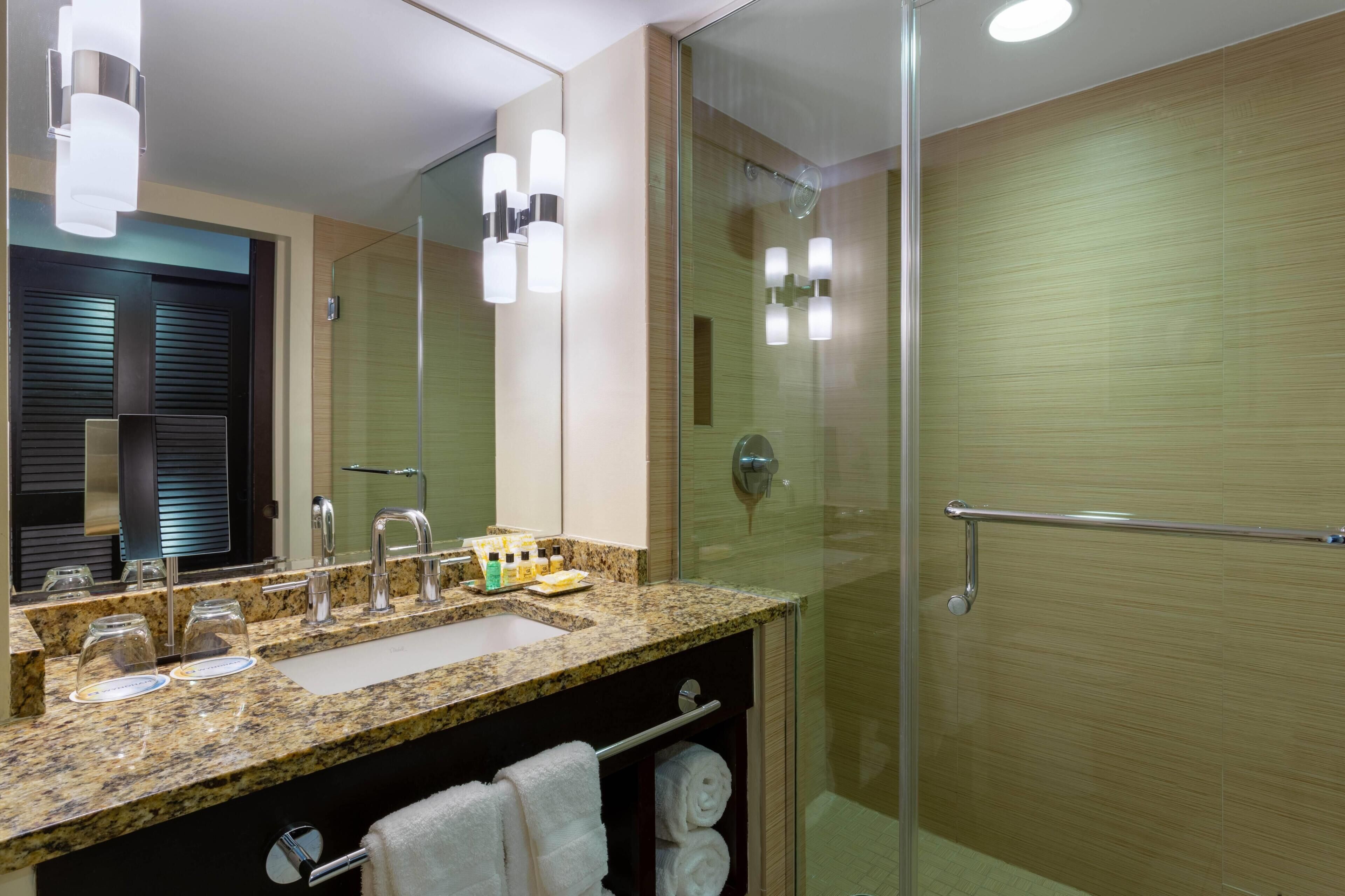 Une salle de bain moderne avec un comptoir en granit, une cabine de douche en verre et un grand miroir.
