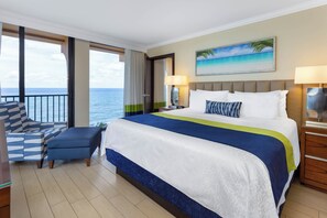 Ein Hotelzimmer mit einem großen Bett, Meerblick, einem Balkon mit einem Stuhl und einem Gemälde, das eine Strandansicht zeigt.