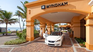 Entrada de un hotel Wyndham, un coche blanco estacionado frente, palmeras y vista a la playa.