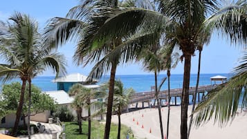 A beach view with palm trees, a pier, and a building with a blue roof.