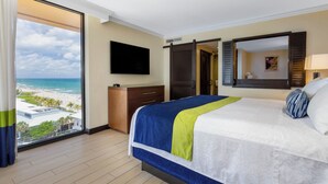 Habitación de hotel con una cama grande, televisión, vista a la playa y una puerta corrediza.