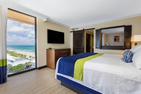 A hotel room with a large bed, a TV, a view of the beach, and a sliding door.