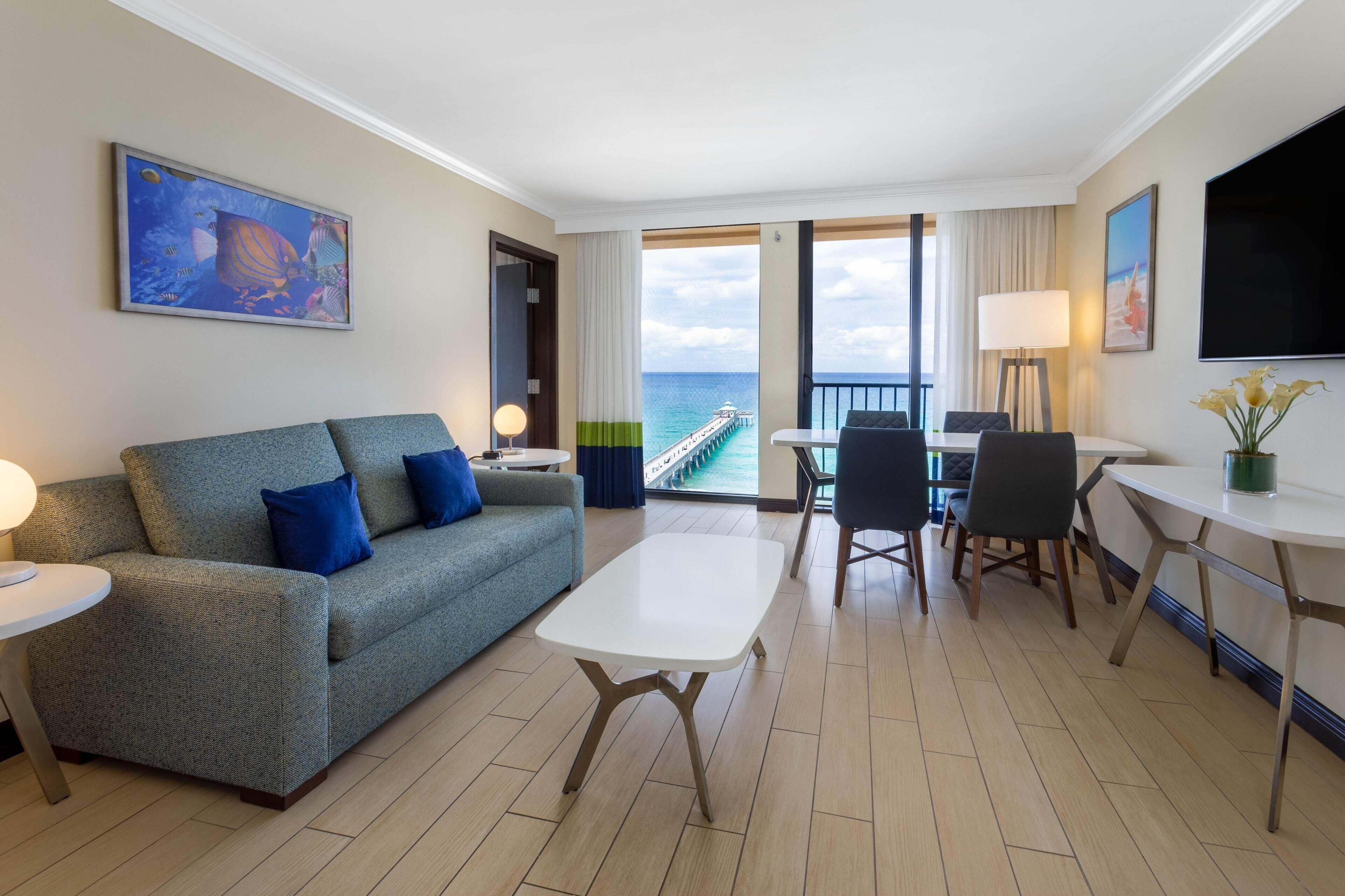 Une chambre d’hôtel avec un balcon, un canapé, une table à manger et un téléviseur.