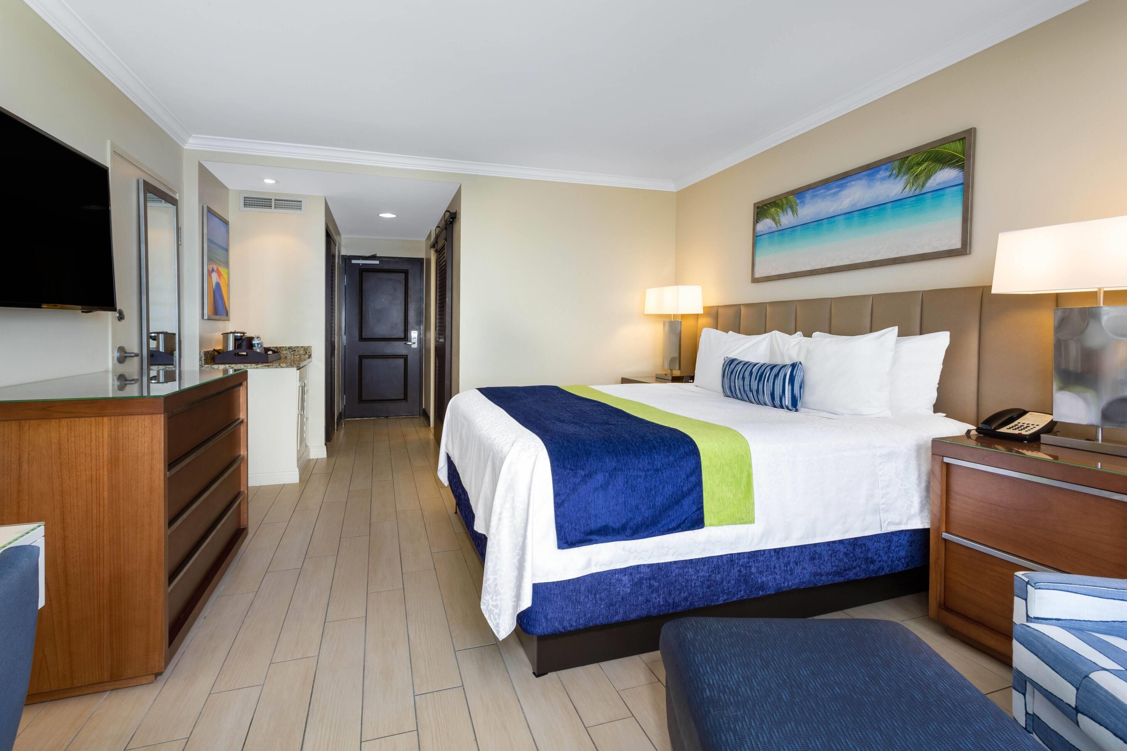 Habitación de hotel con cama, escritorio, silla, televisor y un cuadro en la pared.