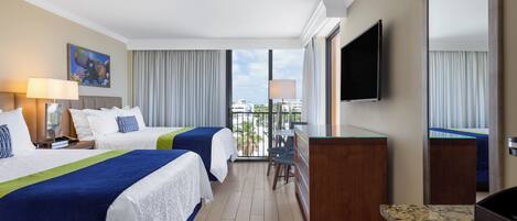 A hotel room with two beds, a desk, a TV, and a balcony with a view.