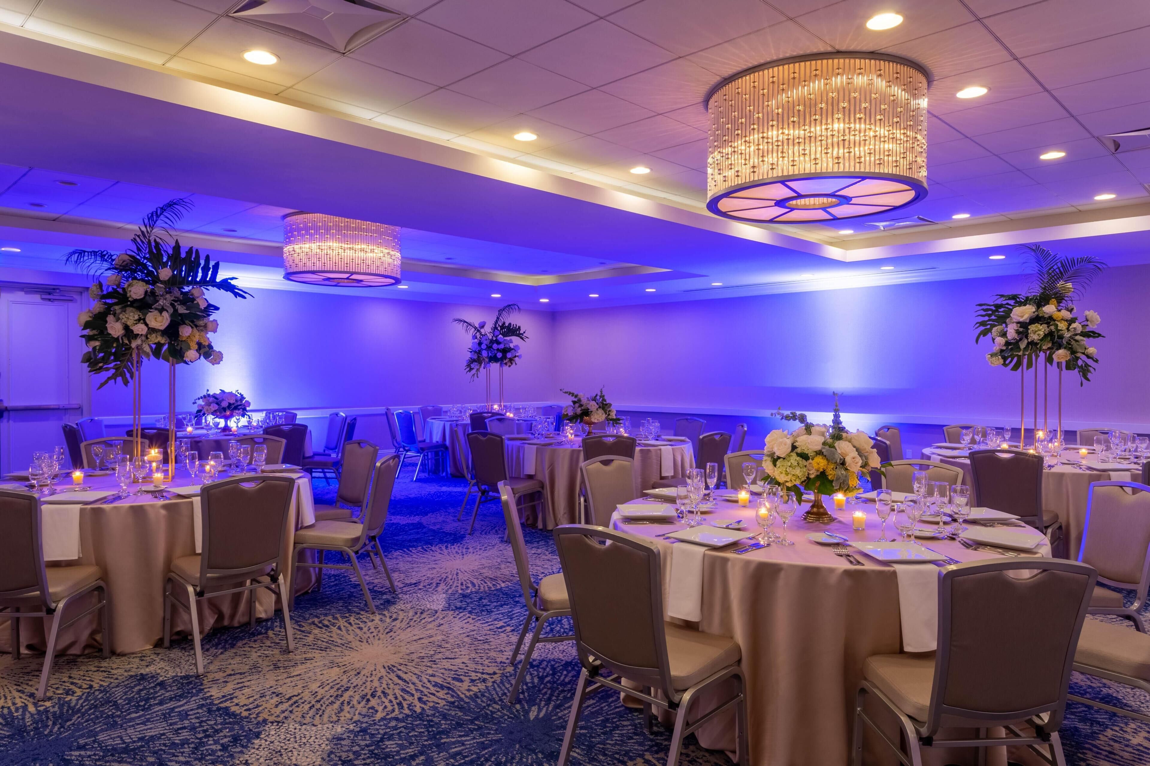 Un salón de banquetes con mesas redondas, sillas y centros de mesa florales.