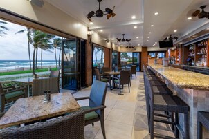 Zona de bar con una barra alargada, asientos con sillas de mimbre y vista a la playa.