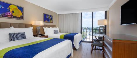A hotel room with two beds, a desk, a TV, and a balcony with a city view.