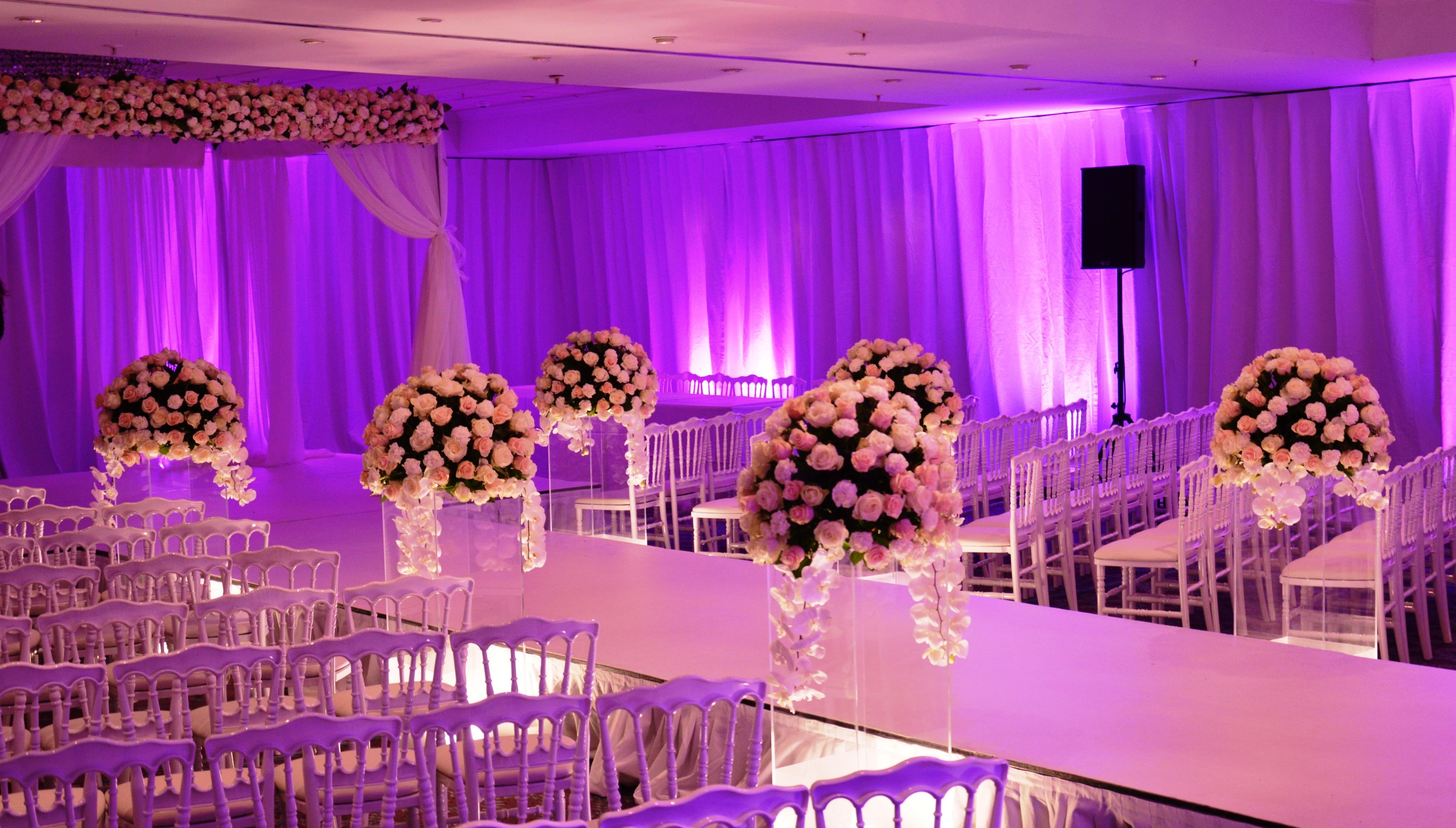 A banquet hall with white chairs, tables, and floral centerpieces.