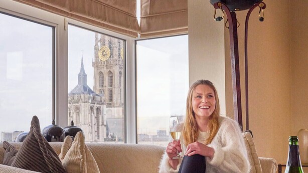 Una persona seduta su un divano beige con vista su un edificio storico attraverso un'ampia finestra.