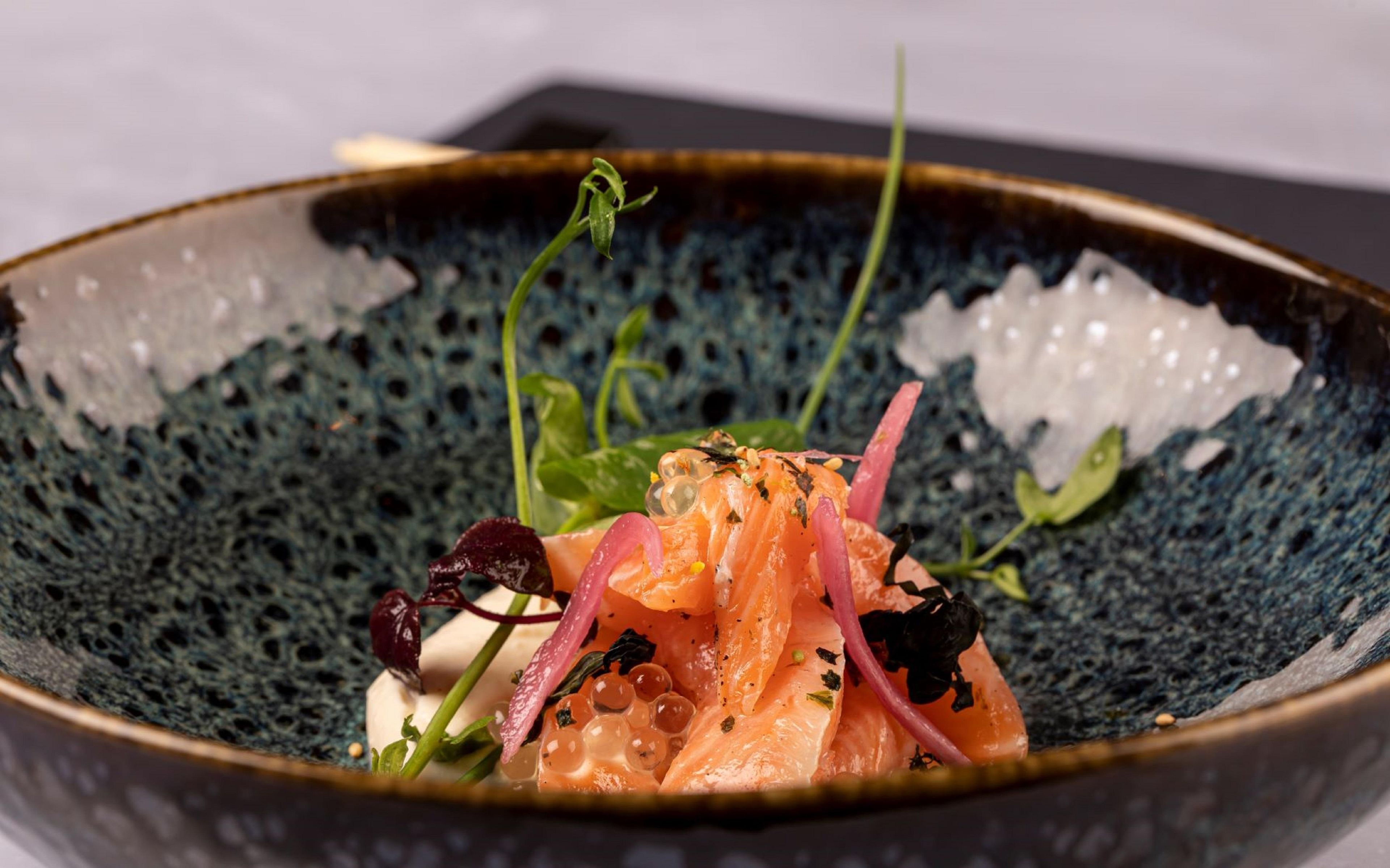 Un plat composé de saumon, de légumes verts et d’un élément décoratif, le tout présenté sur une assiette à texture particulière.